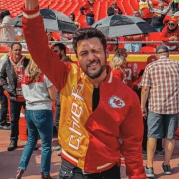 Man in Chiefs jacket celebrating at a sports event with fans in the background