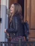 Woman in a leather jacket with a backpack standing in front of a wooden door.