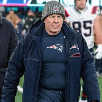 Man wearing a navy jacket with a sports team logo on a football field