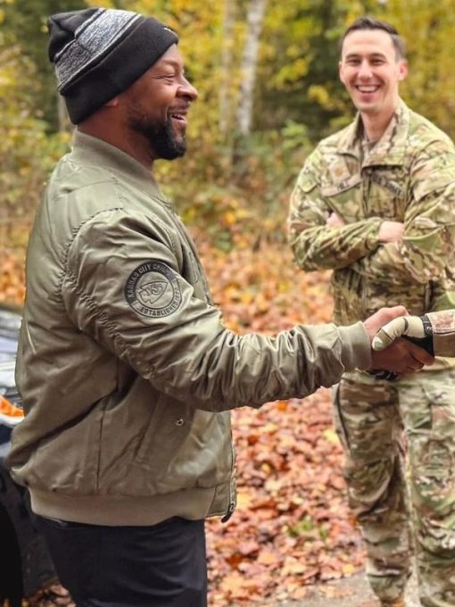 Dante-Hall-Chiefs-Military-Green-2024-Bomber-Jacket-510x680-1 Two men shaking hands outdoors with autumn foliage in the background